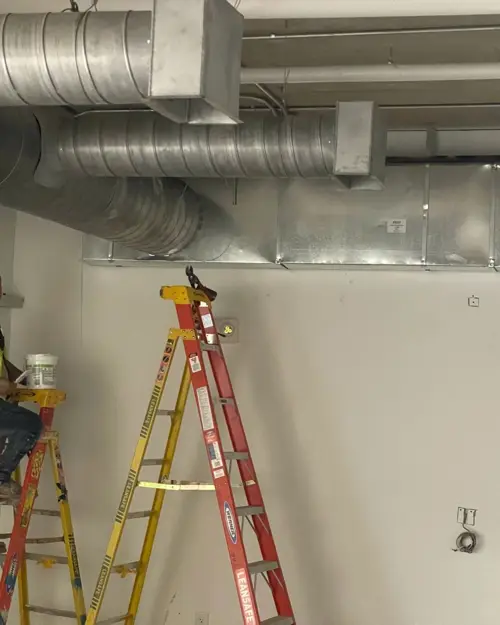 Technician on a ladder under exposed ductwork