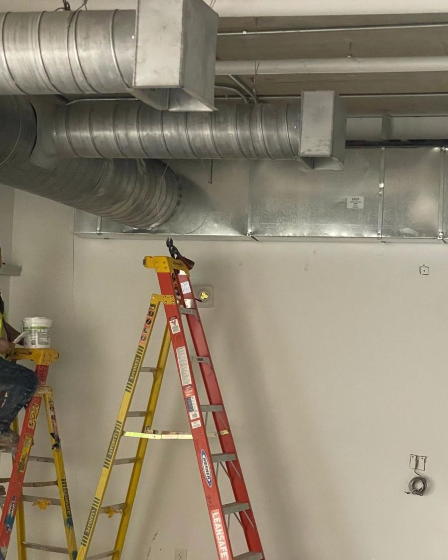 Technician on a ladder under exposed ductwork in a commercial space