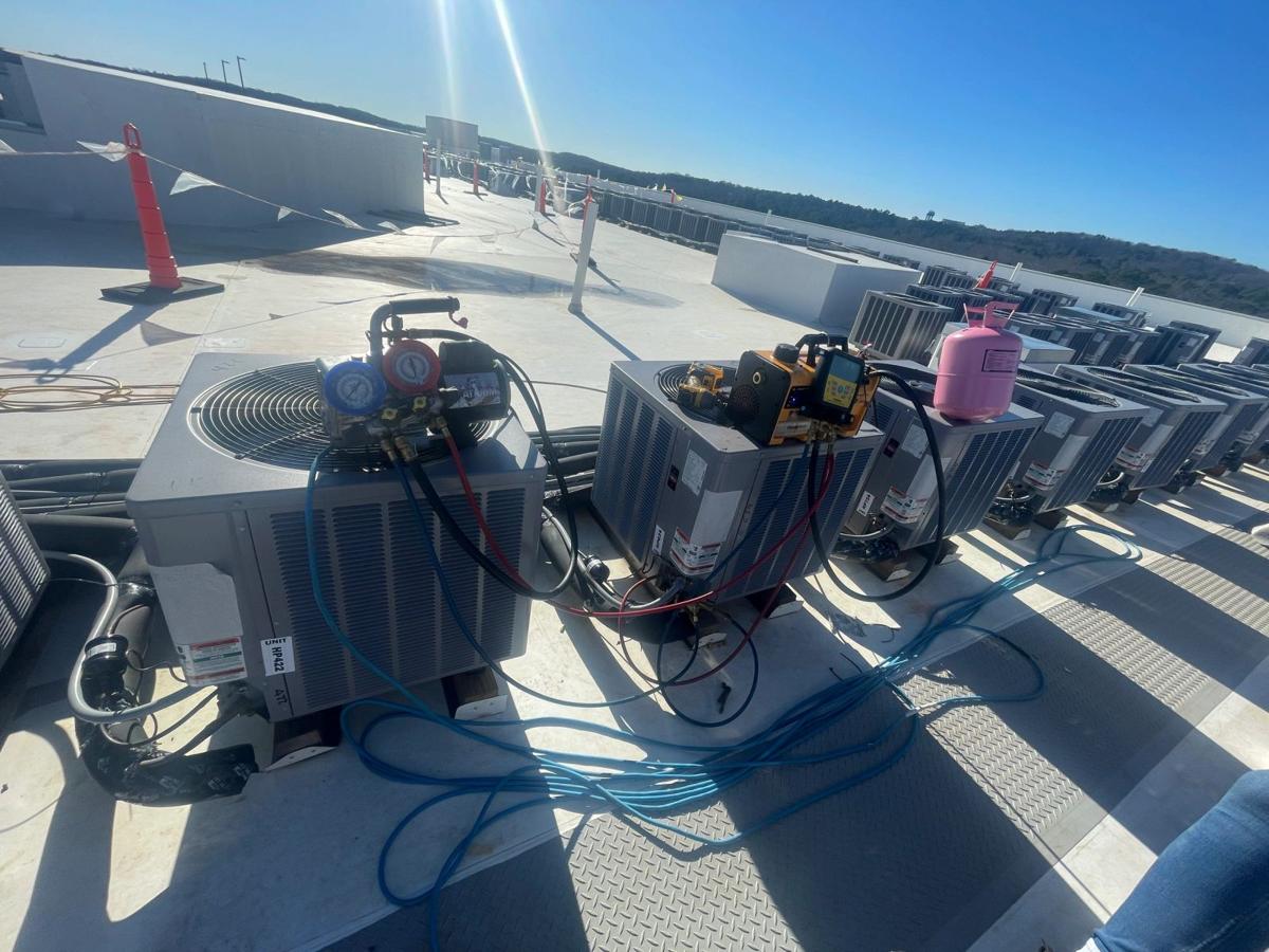 Technician's gauges connected to new condensing units on a rooftop